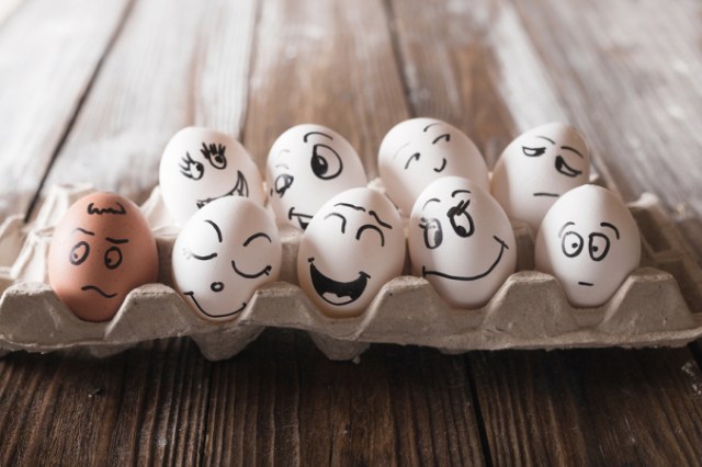 Eggs with funny faces in an open egg carton on wood floor